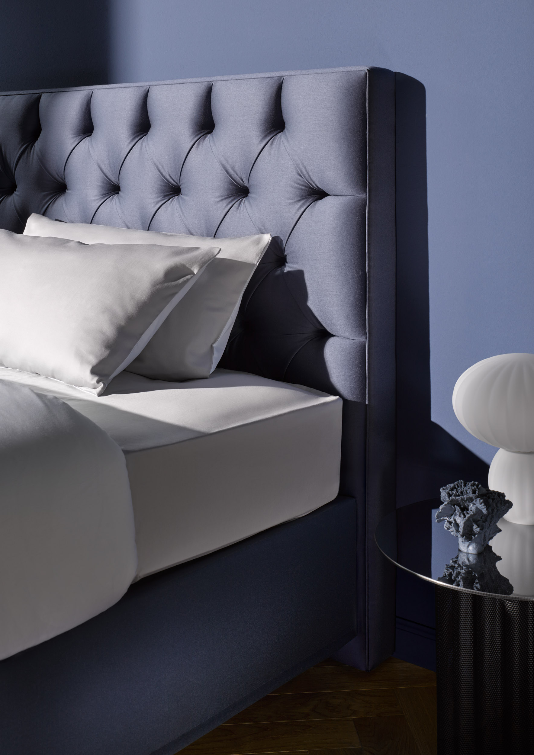 SCHRAMM Bett Origins Basis Kopfteil Elegance Stoff Nicola-3080-indigo Indigo farbenes Kopfteil eines hochwertigen bettes vor blauer wand SCHRAMM Bett Origins Basis Kopfteil Elegance Stoff Nicola bei Betten Leitermann